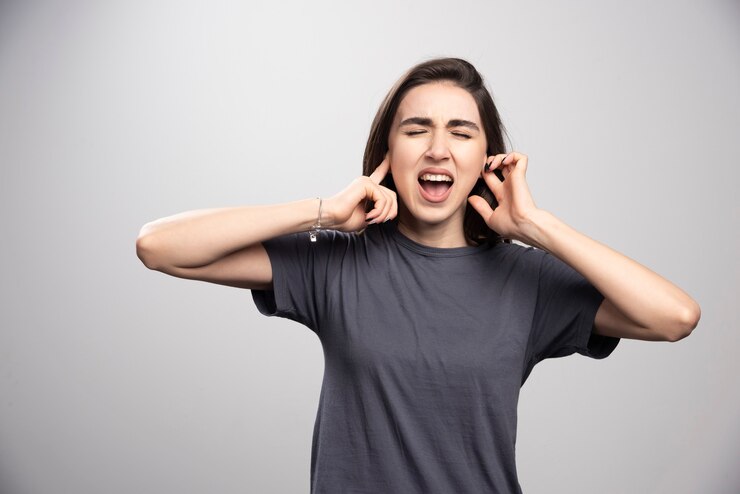 young-woman-covering-her-ears-gray-background_114579-59384