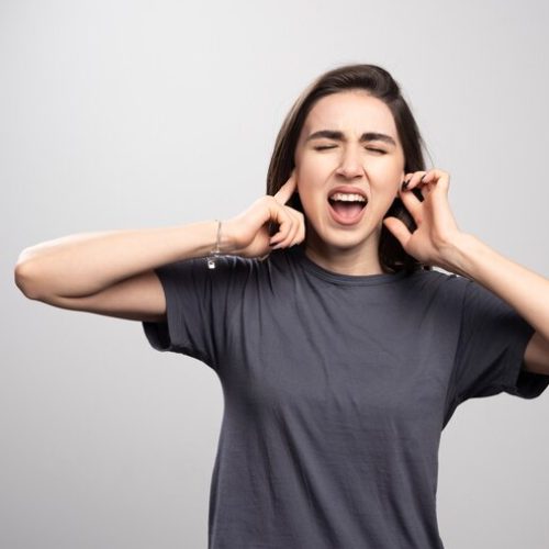 young-woman-covering-her-ears-gray-background_114579-59384