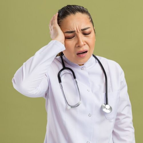 young-woman-doctor-white-medicine-coat-with-stethoscope-around-neck-looking-unwell-touching-her-head-suffering-from-headache-standing-green-wall_141793-100816